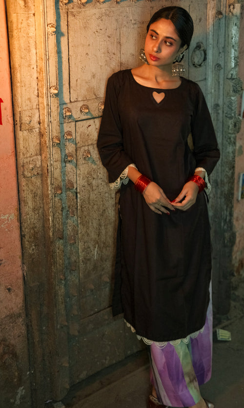 Woman in a dark long-sleeve top and colorful pants standing against a textured wall.